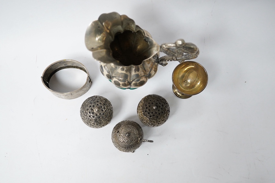 An Indian white metal three piece condiment set, a continental white metal jug, height 14cm, a silver egg cup and an engraved white metal hinged bangle. Condition - poor to fair